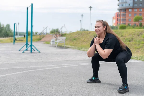 Dicke Mädchen betreiben Fitness auf dem Sportplatz. Schöne junge lächelnde übergewichtige Frau hockt draußen. Schlechte Essgewohnheiten. Übungen auf die Muskeln des Gesäßes. — Stockfoto