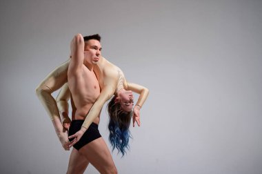 Ağır sirk pozu. Genç bir adam esnek bir kadını tutuyor. Beyaz arka planda poz veren iki akrobat ya da balerin. Bir çift jimnastikçi sanat icra ediyor..