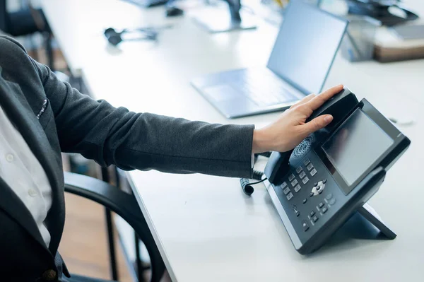 Крупный план женской руки на стационарном телефоне в офисе. Безликая женщина в костюме работает секретаршей, отвечающей на звонки клиентов.. — стоковое фото