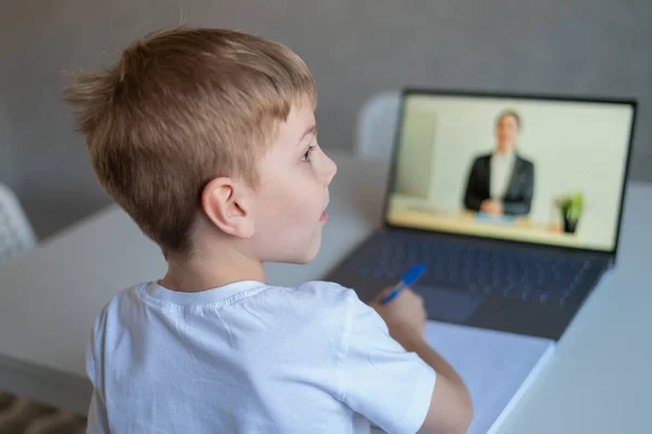 El niño se comunica con una maestra en una webcam portátil. Lección en línea. Educación a distancia en cuarentena. Un escolar está estudiando en casa en la epidemia de coronavirus . — Foto de Stock