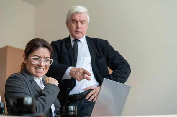 The male boss indicates the female subordinate a mistake. A gray-haired mature business man scolds an employee for unfulfilled work. An upset Caucasian woman failed.