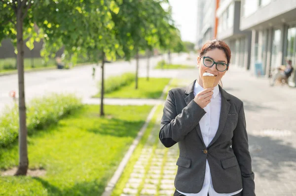 Mujer de negocios camina por la calle y disfruta del helado. Chica feliz en un traje come un cono de helado en un día soleado caliente de verano. Pausa para el almuerzo de un empleado de oficina . —  Fotos de Stock