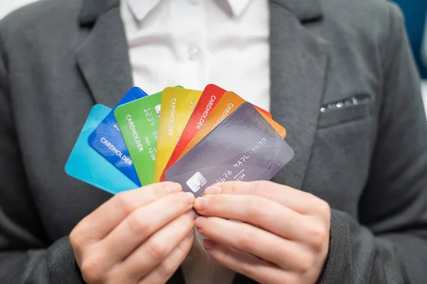 A faceless woman in a suit holds several multi-colored credit cards. A bank employee shows a lot of different plastic cards. Close-up. Lack of cash.