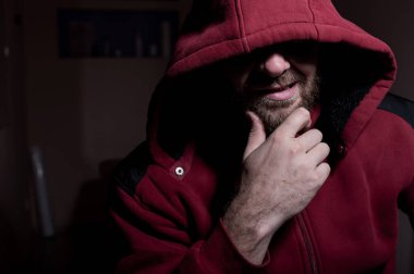 Karanlıkta kapüşonlu kötü sakallı bir adamın portresi. Erkek suçlu gözlerini kaputun altına saklar..