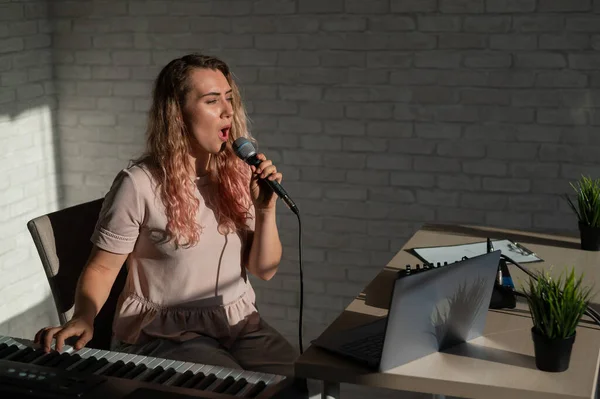 A young European woman sings into a microphone and accompanies on an electronic piano. The girl shoots a video blog. Remote vocal lesson. A female singing teacher conducts online classes.