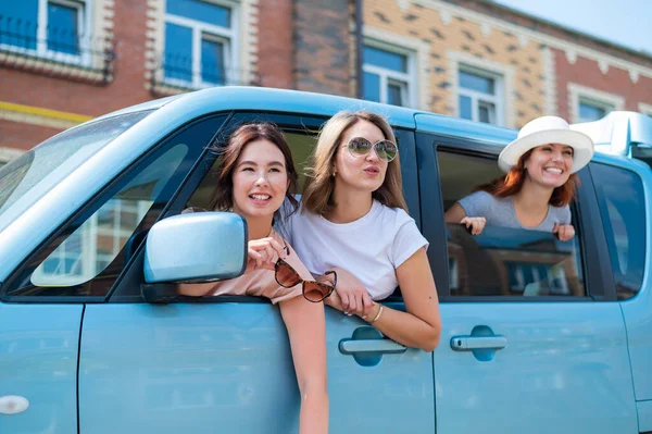 Três namoradas caucasianas alegres olham pela janela do carro. As mulheres excitadas fazem uma viagem de carro. A loira morena e a ruiva vão de férias. — Fotografia de Stock