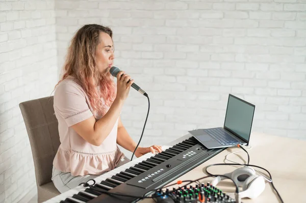 Een vrouw neemt een zangles op met een laptop en begeleidt thuis op een toetsenbord. De leraar zingt een liedje in de microfoon en speelt elektronische piano. Een blogger neemt een video op. — Stockfoto