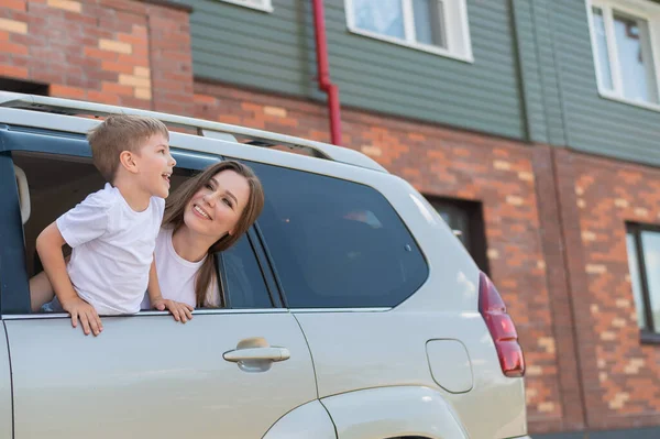 Bütün aileyle arabayla seyahat etmek. Oğlu gülümseyen mutlu beyaz kadın bir cipin arka koltuğunda oturmuş pencereden dışarı bakıyor. Yaz tatilinde araba gezisi. — Stok fotoğraf