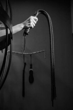 Kafeste uzun, dokunmuş deri kamçılı bir kadın eli. BDSM Ceza ve Zevk. Kırpılmış.