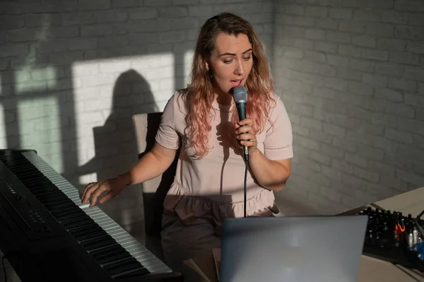 A young European woman sings into a microphone and accompanies on an electronic piano. The girl shoots a video blog. Remote vocal lesson. A female singing teacher conducts online classes.