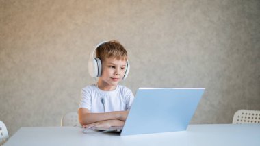 Şirin küçük çocuk dizüstü bilgisayarda çizgi film ya da film izliyor. Beyaz çocuk evde bir masaya oturup kulaklıkla müzik dinliyor..