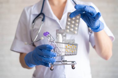 Lastik eldivenli yüzü olmayan kadın doktor tabletlerle su topladı. Küçük bir alışveriş arabası. Eczaneden ilaç alma fikri. Eczane.