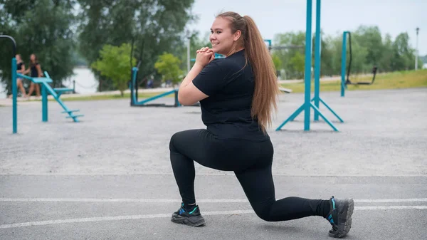 Krásná tlustá dívka v černé teplákové soupravě se zabývá fitness na sportovním hřišti. Mladá žena se vrhá ven za teplého letního dne. Zdravý životní styl a hubnutí. — Stock fotografie