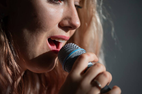 Close-up portrait of a caucasian woman with curly hair singing into a microphone. Beautiful sensual blonde girl is singing a song.