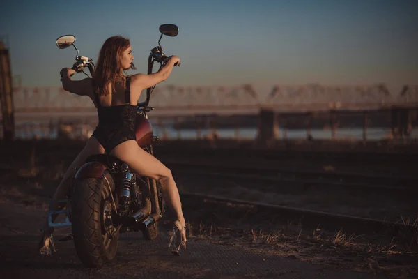 Mulher de cabelos vermelhos em lingerie sexy em salto alto senta-se em uma motocicleta. Atraente menina ruiva senta-se em uma motocicleta ao pôr do sol — Fotografia de Stock