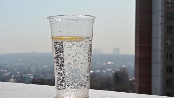 Au ralenti. Une tranche de citron est jetée dans le soda sur le fond de la fenêtre. Préparation d'une boisson rafraîchissante par une chaude journée d'été. — Video