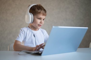 Sevimli Avrupalı çocuk kulaklıkla müzik dinliyor ve dizüstü bilgisayarında yazı yazıyor. Çocuk bilgisayarda ev ödevi yapıyor. Genç bir okul çocuğu uzaktan eğitim alır..