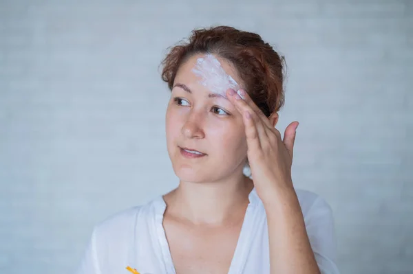 Vitiligo. Portrait of a woman with lack of skin pigmentation on her forehead. Girl smears sunscreen on a white spot on the skin of the face. Autoimmune disease.