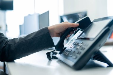 Ofisteki ev telefonunda kadın eli var. Takım elbiseli meçhul kadın müşteri aramalarına cevap veren resepsiyonist olarak çalışıyor..