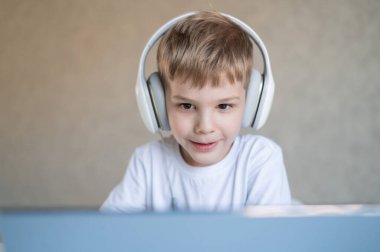 Şirin küçük çocuk dizüstü bilgisayarda çizgi film ya da film izliyor. Beyaz çocuk evde bir masaya oturup kulaklıkla müzik dinliyor..