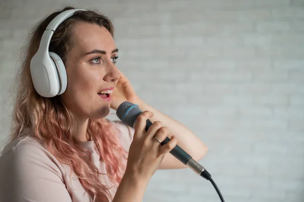 Close-up portret van een blanke vrouw met krullend haar die in een microfoon zingt. mooi sensueel meisje in wit hoofdtelefoon zingt een lied in huis karaoke. — Stockfoto
