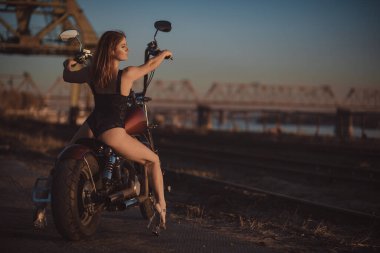 Yüksek topuklu seksi iç çamaşırlı kızıl saçlı kadın motosiklette oturuyor. Çekici kızıl saçlı kız gün batımında motosiklette oturuyor.