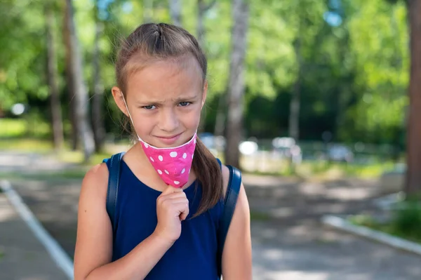 Nešťastná školačka si sundá ochrannou masku venku. Nespokojená dívka nechce v parku nosit masku a sundá si ji.. — Stock fotografie