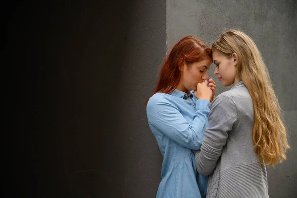 Passionerat kärleksfullt lesbiskt par. Två vackra unga kvinnor kramas ömt utomhus mot en grå vägg. HBTQ-kommun. Flickor på dejt. — Stockfoto