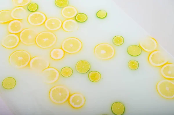 Eau savonneuse trouble dans le bain avec des tranches de citron et de citron vert vue de dessus en plein cadre. Des agrumes. Spa avec lait dans le bain pour le rajeunissement. — Photo