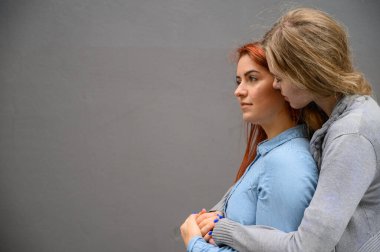 İki mutlu kız arkadaş gri bir duvarın arkasında sarılıyorlar. Lezbiyen bir bayana nazikçe sarılmak. LGBT Eşcinsel Evliliği.