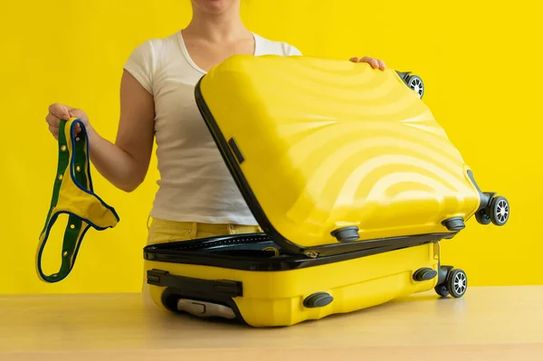 Μια απρόσωπη γυναίκα διπλώνει μπικίνι σε μια βαλίτσα σε κίτρινο φόντο. Το κορίτσι πακετάρει τις αποσκευές για ένα ταξίδι στη θάλασσα. Διακοπές. — Φωτογραφία Αρχείου