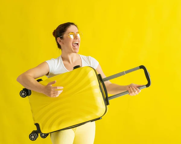 漂亮的高加索女人拿着一个黄色背景的手提箱鬼混。一个迷人的女孩模仿弹吉他.前头旅程的喜悦. — 图库照片