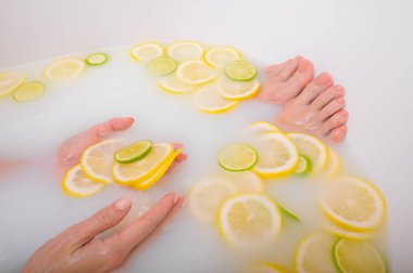 Meçhul, güzel bir kadın süt limonları ve limonla banyo yapıyor. Kesilmiş fotoğraf. Cilt beyazlatıcı banyoda kadın eli ve ayaklarının yakın çekimi.