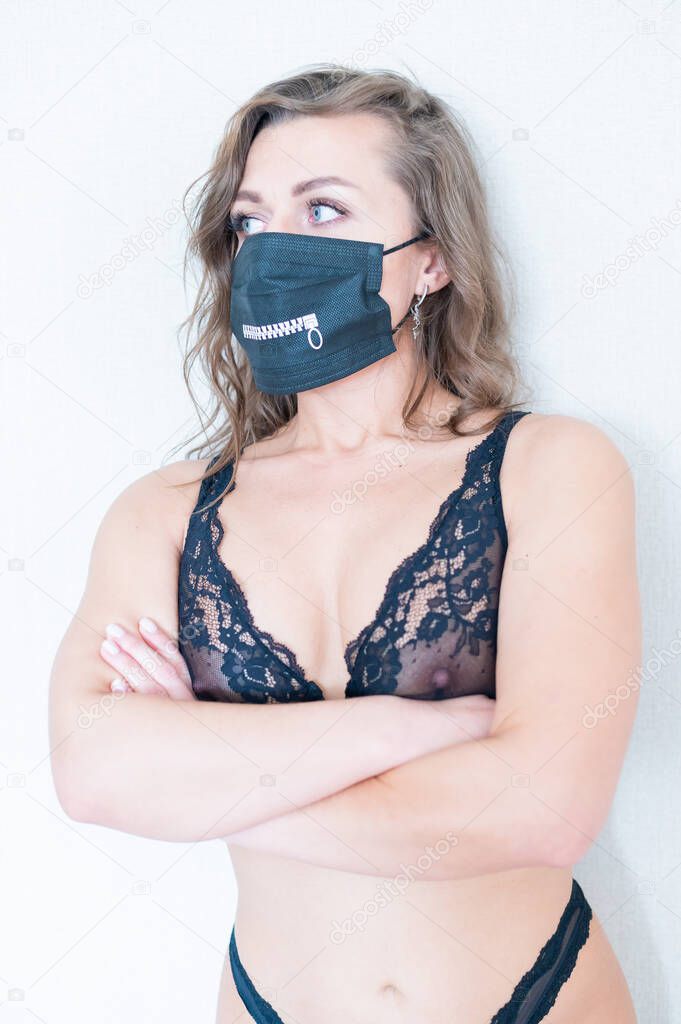 Portrait of a beautiful young woman in black lace lingerie and a protective mask. Sexy naked girl on a white background. Stay home. Quarantine due to coronavirus.