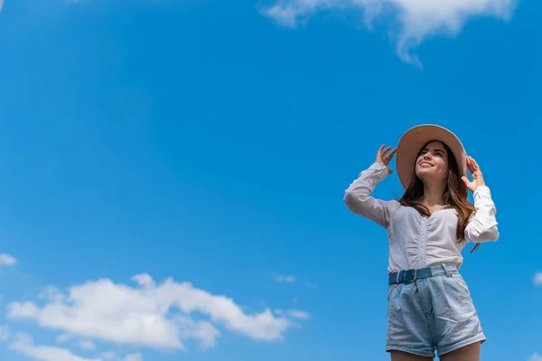 Retrato de una hermosa mujer caucásica al aire libre sobre un fondo azul del cielo. Una chica con sombrero y pantalones cortos en un caluroso día de verano. —  Fotos de Stock