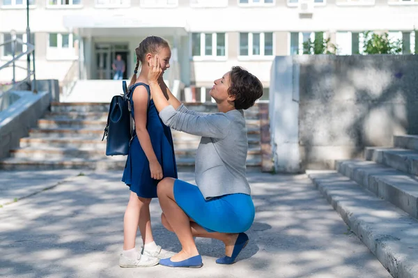 Una madre premurosa prepara sua figlia a scuola. Una bella donna caucasica si accovaccia accanto a una bambina e la manda a studiare. Madre conduce una bambina in prima elementare. — Foto Stock