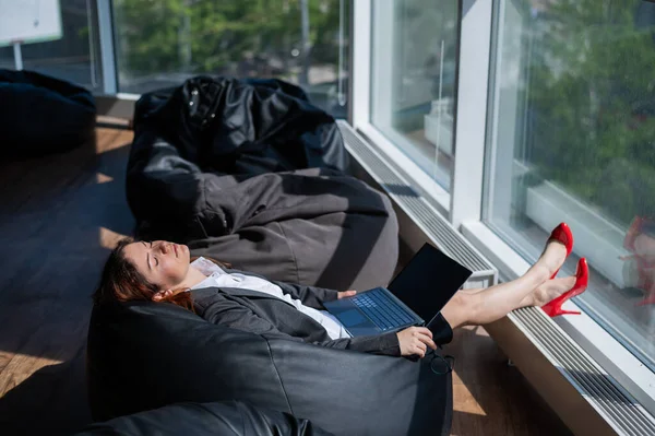 La dama de negocios duerme sentada en una moderna oficina cómoda bolsa de silla bob. Una mujer con traje se quedó dormida en el trabajo en un portátil. El cuidado de la comodidad y la comodidad de los empleados . —  Fotos de Stock