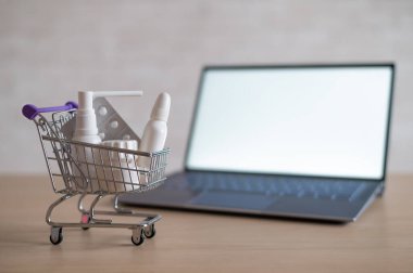 Boş beyaz ekranlı dizüstü bilgisayar ve ilaçlarla dolu minyatür alışveriş arabası. Çevrimiçi eczane kavramı. Tablet satın almak için web sitesi.