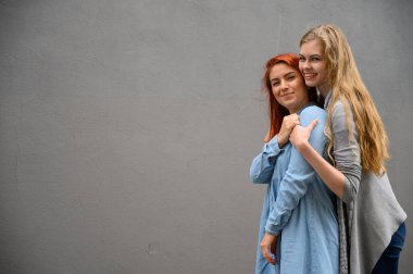 İki mutlu kız arkadaş gri bir duvarın arkasında sarılıyorlar. Lezbiyen bir bayana nazikçe sarılmak. LGBT Eşcinsel Evliliği.