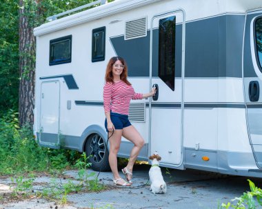 Güzel beyaz kadın karavanın yanında bir köpeği eğitiyor. Hayvanınla seyyar bir karavanla seyahat et. Kadın karavan sürücüsü.