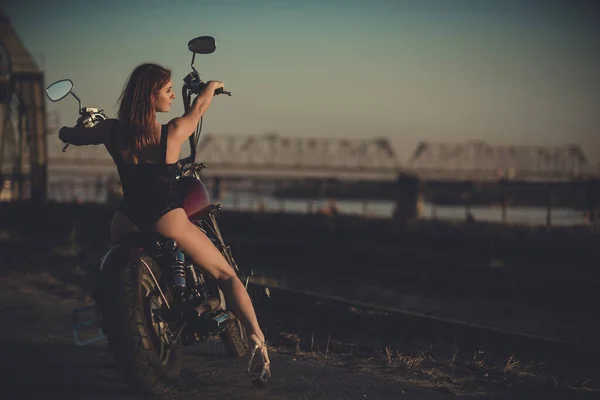 Donna dai capelli rossi in lingerie sexy con i tacchi alti siede su una moto. Attraente ragazza dai capelli rossi siede su una moto al tramonto — Foto Stock