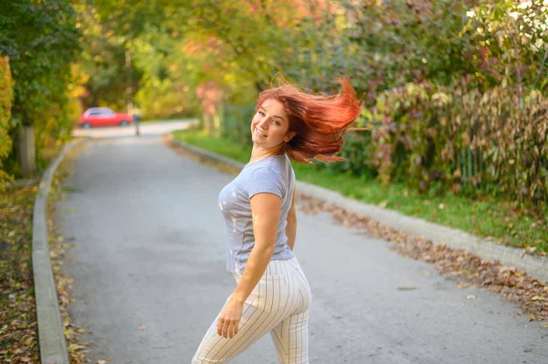 Eine schöne rothaarige Frau spaziert an einem warmen Herbsttag durch den Park. Das Mädchen dreht sich um. — Stockfoto