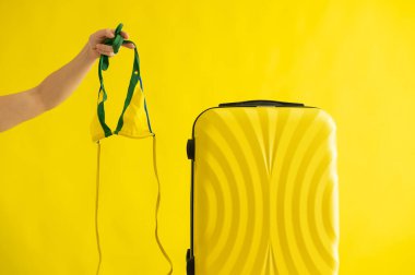 Yüzü olmayan bir kadın, sarı arka planda bir bavulun yanında bikiniyle geziye çıkıyor. Bir kadın el yaz tatili için mayo hazırlıyor. Boşluğu kopyala.