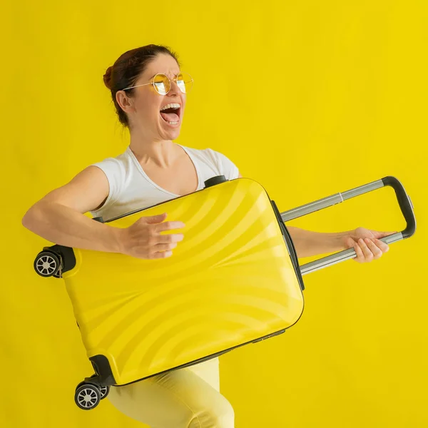 漂亮的高加索女人拿着一个黄色背景的手提箱鬼混。一个迷人的女孩模仿弹吉他.前头旅程的喜悦. — 图库照片