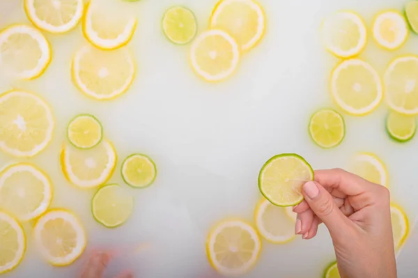 Close-up of a female hand holding a slice of citrus fruit in a milk bath. — Stock Photo, Image