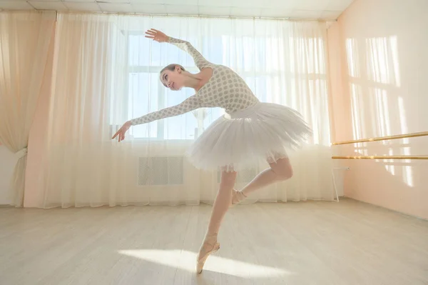 Vacker graciös ballerina övar i hallen mot bakgrund av ett fönster. Smal kvinna i tutu och tåskor i en dansklass. — Stockfoto