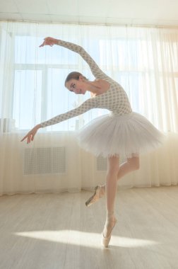 Güzel zarif balerin salonda bir pencerenin arkasında prova yapıyor. Tutu giymiş ince bir kadın ve dans sınıfındaki sivri ayakkabılar..