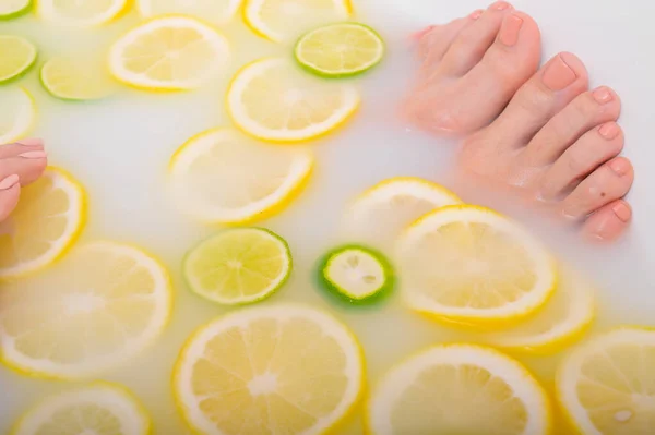 Fille prend un bain de lait avec des citrons et des citrons verts. Spa aux agrumes. Soins du corps. Blanchiment de la peau. Femmes pieds. — Photo