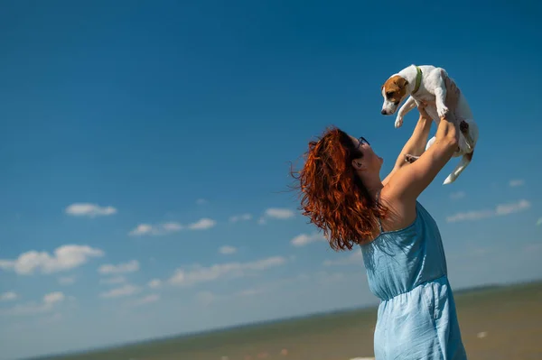 Счастливая женщина обнимается с собакой у моря. Рыжая белая девушка держит щенка Джека Рассела Терьера. Любовь между домашним животным и владельцем. — стоковое фото