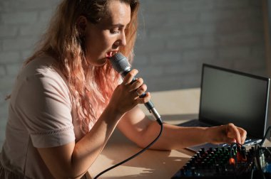 Bir kadın mikrofona şarkı söylüyor ve internetten çalıyor. Bir kadın blogcu dizüstü bilgisayarlı bir sentezleyici kullanarak şarkı kaydediyor..